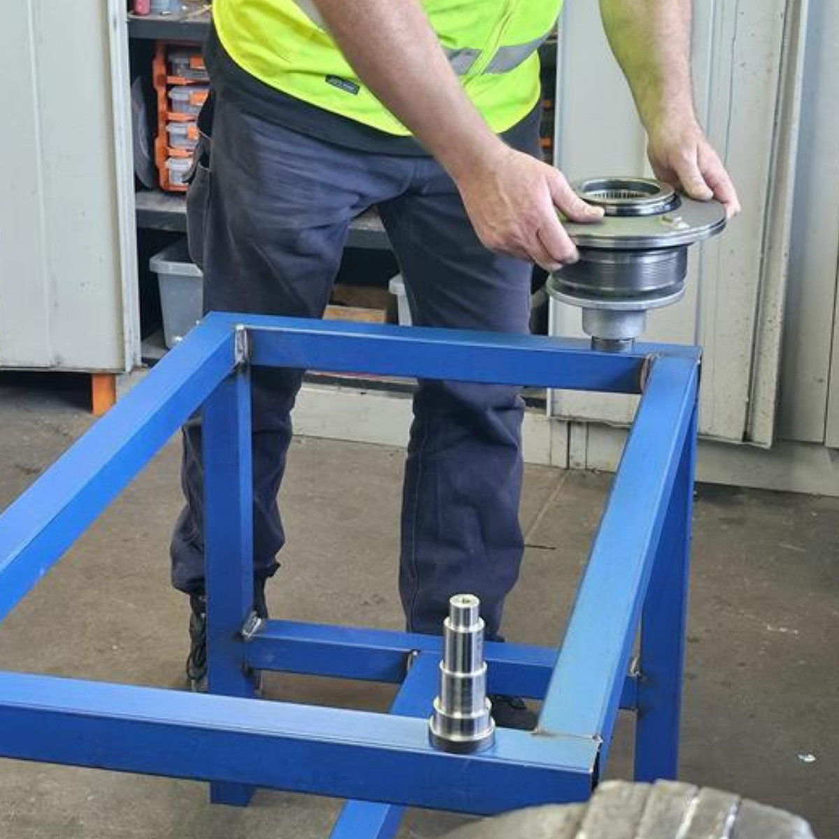 A man assembles metal pieces on a large blue metal frame.